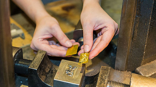 Zwei Hände halten zwei kleine Goldplatten, in die ein Motiv eingestanzt ist.