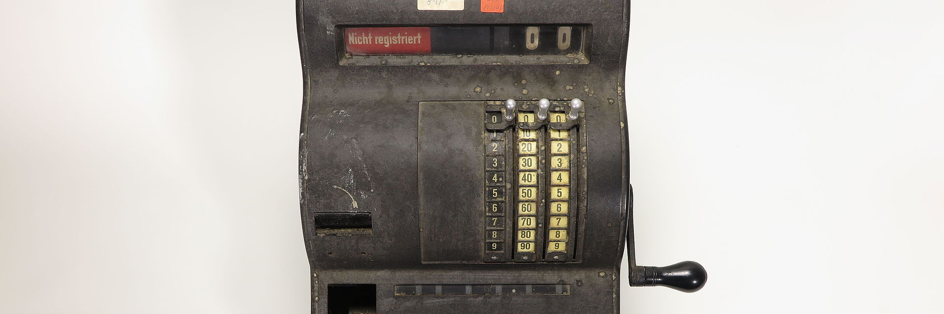 Registrierkasse aus den 1930er Jahren mit vier farbigen Aufklebern der KuA. Die Aufkleber tragen Zahlen und Buchstaben.