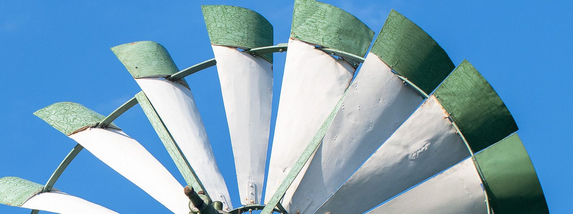 Weiß-grüne Flügelblätter eines Windrads vor blauem Himmel.