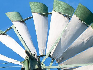 Weiß-grüne Flügelblätter eines Windrads vor blauem Himmel.