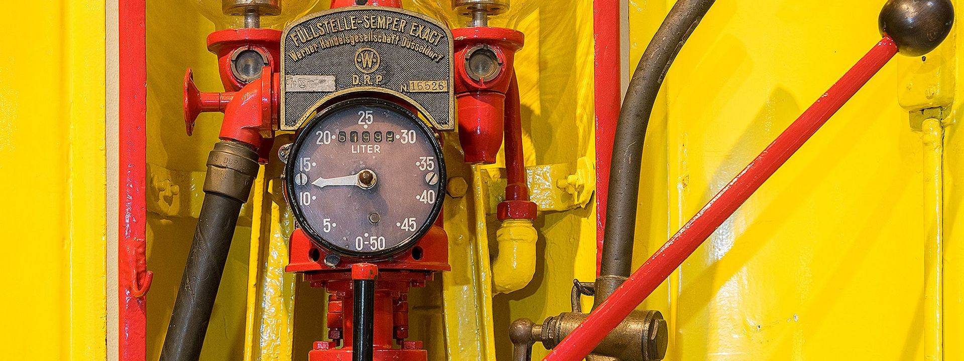 Eine gelbrote Zapfanlage. Die analoge Anzeige in der Mitte steht zwischen 10 und 15, auf der Metallplakette darüber steht „Füllstelle-Sempler Exact“