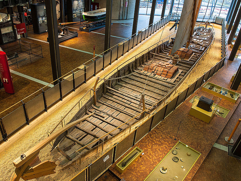 Der Kaffenkahn ist ein hölzernes Schiff, dessen Bodenplanken bis zur Wasserlinie aufgebogen sind. Am Heck des schlanken Kahns sind das Ruder und die Pinne zu erkennen.