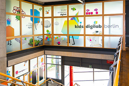 Ansicht von der Innentreppe auf Glasfassade der oberen Etage des kids.digilab und unteren Eingang des kids.digilab.