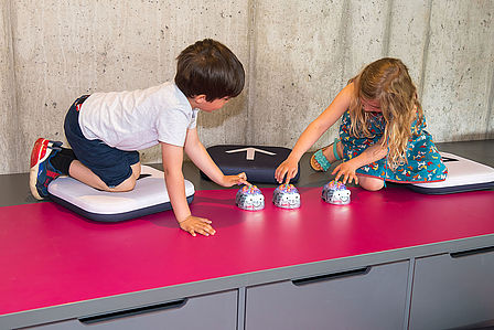 Zwei Kinder drücken die Startknöpfe mehrerer Robotik-Spielzeuge, die wie gläserne Mäuse aussehen.