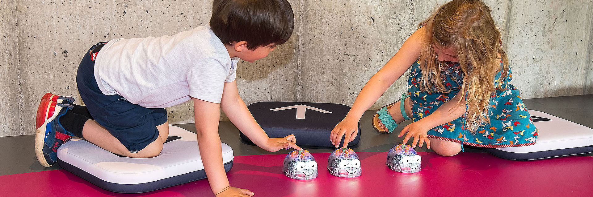 Zwei Kinder drücken die Startknöpfe mehrerer Robotik-Spielzeuge, die wie gläserne Mäuse aussehen.