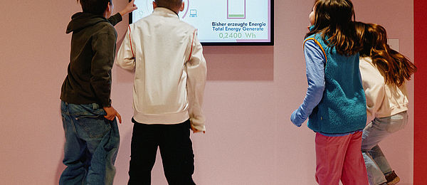 Zwei Mädchen und zwei Jungen hüpfen fröhlich in die Luft. Vor ihnen ein Display, das anzeigt, wie viel Energie sie dabei erzeugen.