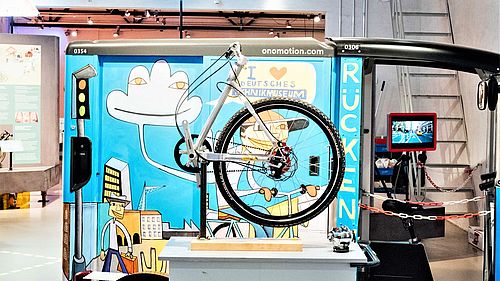 Im Bild ein buntes e-Lastenrad, davor aufgebauter Workshoptisch.