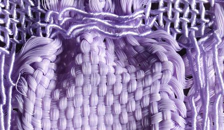 Detailaufnahme eines lilafarbenen Gewebes. Durch zwei unterschiedlich elastische Garne, Gummilitze und Seide, tritt das Blasenmuster des Stoffes besonders hervor. 