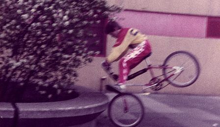Ein Junge auf einem BMX-Rad vollführt ein Kunststück, bei dem das Hinterrad in der Luft schwebt.