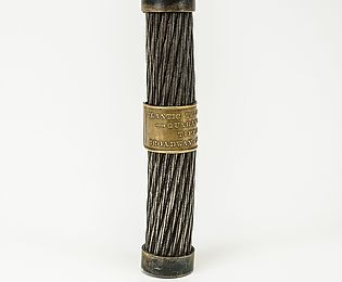 Vor hellem Hintergrund steht ein kleines Stück des ersten Transatlantikkabels. Darauf eine bronzene Banderole mit der Aufschrift "Tiffany & Co.".