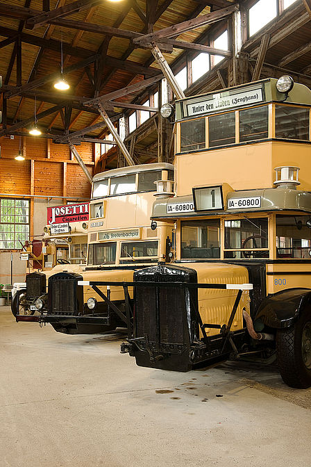 Die historischen gelben Busse stehen aufgereiht im Depot für Straneverkehr des Deutschen Technikmuseums in der Monumentenhalle.
