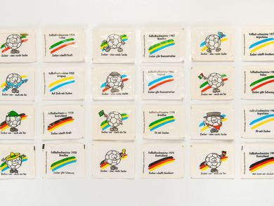24 weiße rechteckige Zuckertütchen sind chronologisch in der Reihenfolge ihres Fußballweltmeister-Titels sortiert. Sie sind bedruckt mit Motiven wie Fußbällen, die landestypische Hüte tragen oder Fahnen schwenken sowie den jeweiligen Nationalfarben der jeweiligen Weltmeister und Werbesprüchen wie „Zucker – eine runde Sache“ oder „Zucker schafft Ausdauer“.