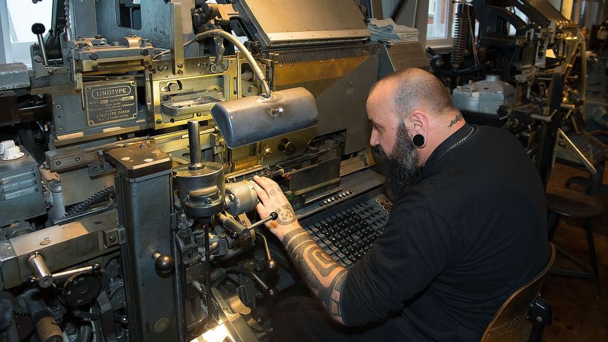Ein Mann arbeitet an einer großen, schwarzen Setzmaschine. 