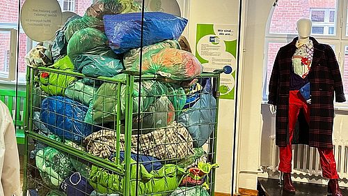In der Ausstellung Textiltechnik steht ein Metallcontainer mit Kleiderspendesäcken