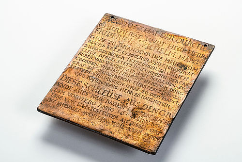 Die Tafel aus Kupfer hat etwa die Maße und das Gewicht eines kleinen Tabletcomputers. In der gewellten und mit Furchen überzogenen Oberfläche ist ein Text eingraviert, der in frühem Neuhochdeutsch vom Bau der Berliner Schleuse im Jahr 1657 berichtet.