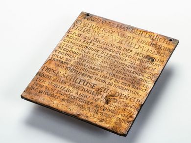 Die Tafel aus Kupfer hat etwa die Maße und das Gewicht eines kleinen Tabletcomputers. In der gewellten und mit Furchen überzogenen Oberfläche ist ein Text eingraviert, der in frühem Neuhochdeutsch vom Bau der Berliner Schleuse im Jahr 1657 berichtet.