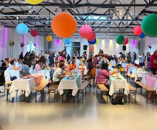 In der Ladestraße, Halle 5, wird eine Kinderveranstaltung gezeigt. Die Bierzeltgarnituren sind bunt dekoriert und von der Decke herab hängen große bunte Ballons. 