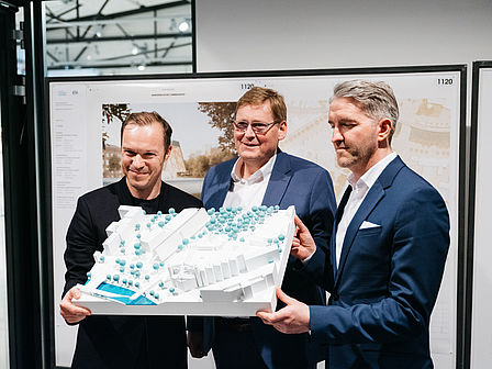 Drei Männer halten ein Architekturmodell hoch.