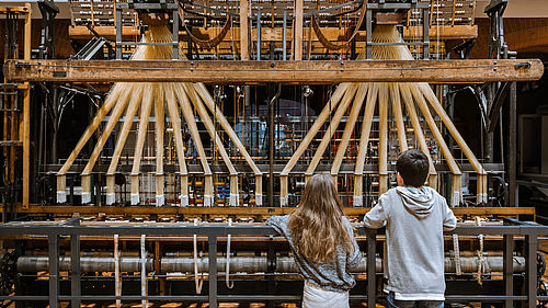 Zwei Kinder stehen vor dem historischen Bandwebstuhl im Foyer des Museums.