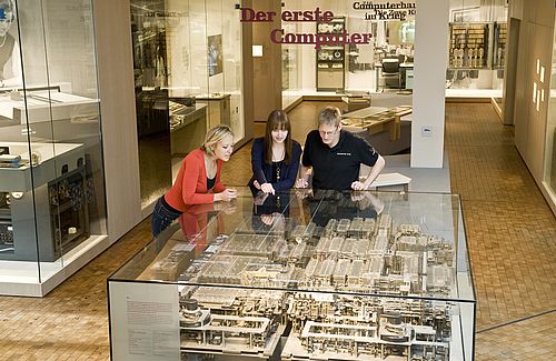 Zwei Frauen und ein Mann beugen sich über eine große Glasvitrine, in der das mechanische Rechenwerk der Z1 zu sehen ist.