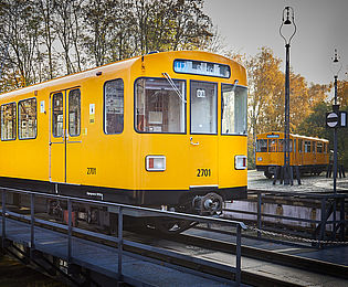 Blick auf einen orangenen U-Bahnwagen, der im Freien auf einer Drehscheibe steht. Die Formen sind rundlich.