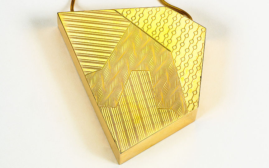 Kette mit asymmetrischem Fünfeck aus Messing als Anhänger. Die Oberfläche ist in vier Felder geteilt, die mit verschiedenen Linienmustern verziert sind.