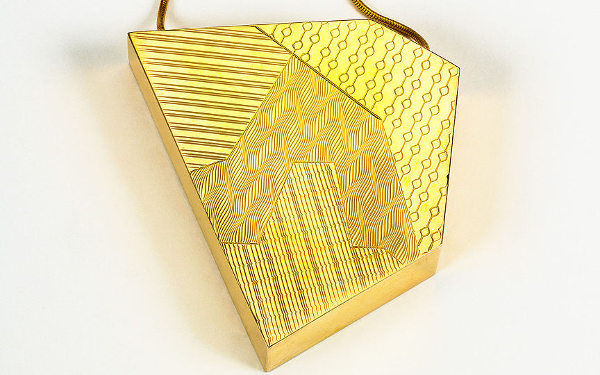 Kette mit asymmetrischem Fünfeck aus Messing als Anhänger. Die Oberfläche ist in vier Felder geteilt, die mit verschiedenen Linienmustern verziert sind.