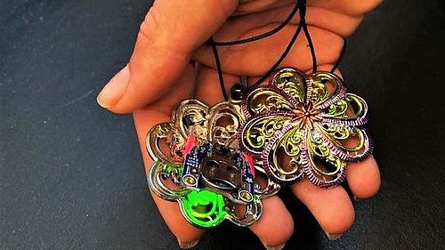 Eine Hand hält ein bemaltes Zinngussamulett, das durch eine eingelöteten LED grün leuchtet