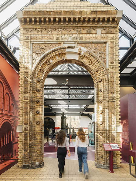 Zwei Frauen laufen auf ein altes, reich verziertes Portal zu, das sogenannte Fürstenportal des Anhalter Bahnhofs. Im Hintergrund ist die Ausstellung Schienenverkehr zu erkennen.