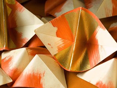 Eine Vielzahl gefalteter Papierschiffchen. Das Papier der Schiffchen verläuft von den entgegenliegenden Außenkanten zur Mitte von weiß nach rot. Die Faltmitte ist mit Goldblatt veredelt.