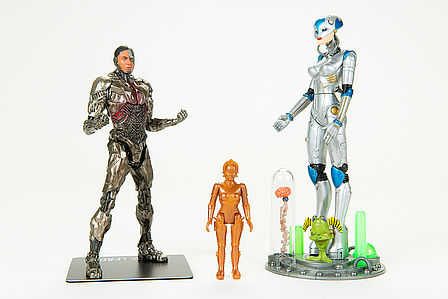 Zwei große Figuren aus Kunststoff an den Seiten, eine kleine Figur in der Mitte. 