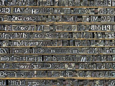 Viele verschiedene Drucktypen - erhabene, spiegelverkehrte Buchstaben aus Blei - liegen in einem Setzkasten nebeneinander. 