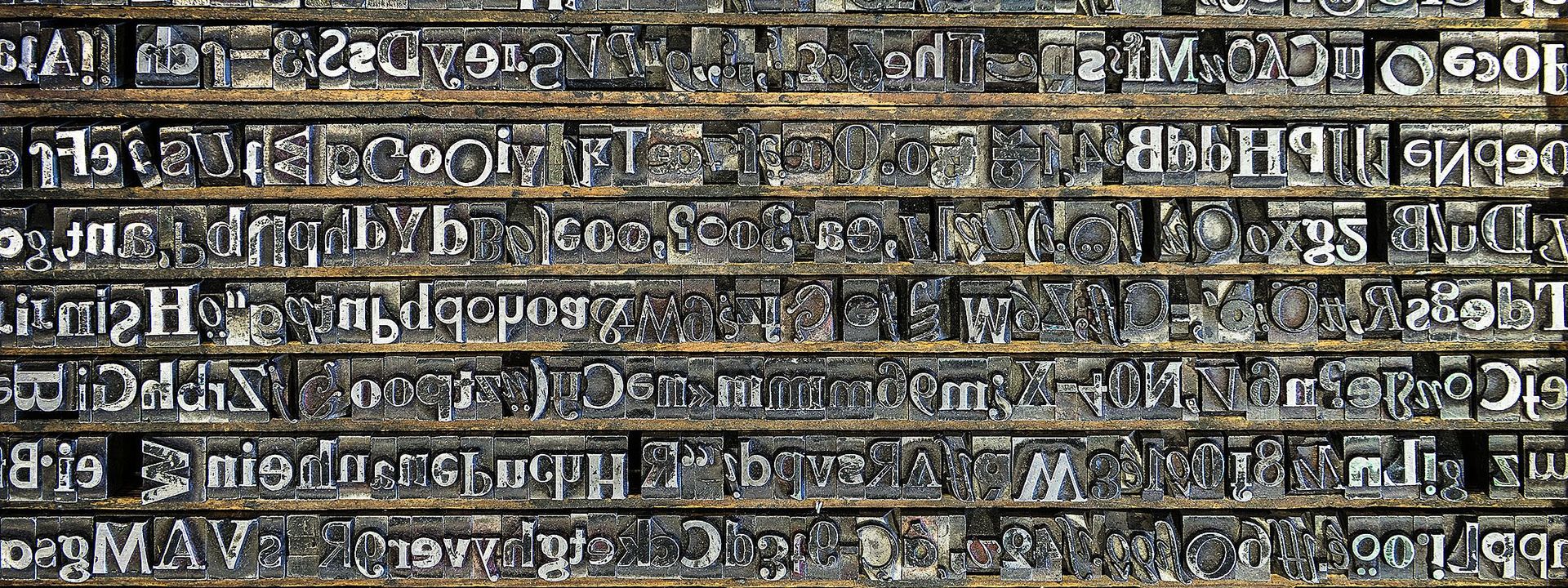 Viele verschiedene Drucktypen - erhabene, spiegelverkehrte Buchstaben aus Blei - liegen in einem Setzkasten nebeneinander. 