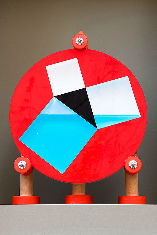 Foto einer Experimentier-Station. Auf einer drehbaren Scheibe befindet sich ein recht-winkliges Dreieck, an dessen Seiten jeweils ein Quadrat anschließt. Eine blaue Flüssigkeit füllt die Fläche hinter den zwei kleinen Quadraten aus.