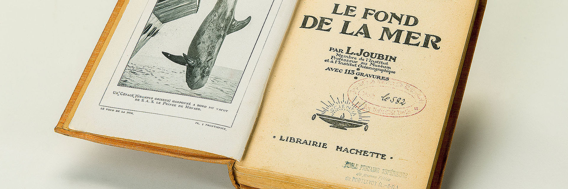 Auf der Titelseite eines aufgeschlagenen Buches sind mittig unter der Überschrift „Le fond de la mer“, französisch für „Der Meeresboden“ Abdrücke von zwei Bibliotheksstempeln zu erkennen.
