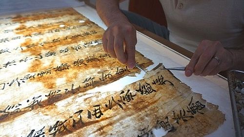 Auf einem Leuchttisch wir eine Karte mit asiatischen Schriftzeichen repariert.