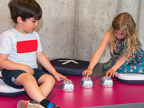 Zwei Kinder lernen in den farbenfrohen Räumen des kids.digilab mithilfe von Robotikspielzeug zu denken und zu spielen wie ein Computer.