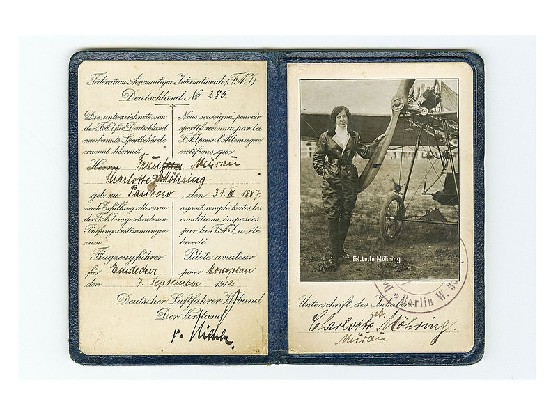 Flugzeugführerschein, aufgeklappt. Die personenbezogenen Daten wurden mit schwarzer Tinte handschriftlich auf der linken Seite eingetragen. Die rechte Seite enthält ein Schwarzweiß-Foto einer Frau vor einem Flugzeug. Unterhalb des Fotos befindet sich die Unterschrift von Frau Charlotte Möhring und ein Stempel.