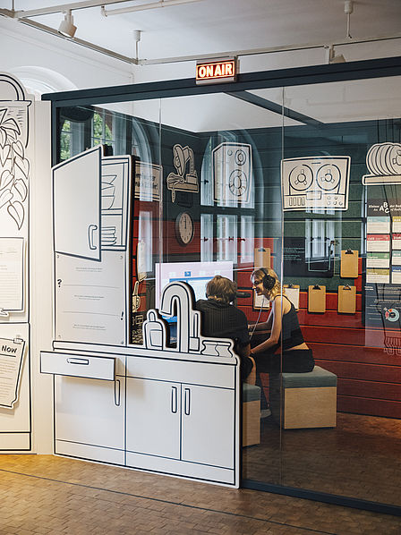 Blick in das gläserne Studio im Ausstellungsbereich "Radio Gleisdreieck". Im Studio sind zwei Personen zu erkennen. Über dem Eingang zum Studio leuchtet der Schriftzug "On Air".