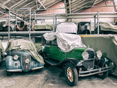 Blick in das Depot des Museums, in dem Automobile nebeneinander und in speziellen Hochregalen stehen. Vor Schmutz und Staub sind die Fahrzeuge durch eigens geschneiderte Stoffhauben geschützt.