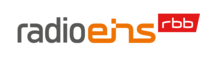 Das Logo des Senders radio eins. Der Schriftzug "radio" in Grau, "eins" in Orange und daneben hochgestellt "rbb" in Weiß auf rotem Grund.