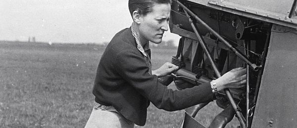 Das Schwarz-Weiss-Foto zeigt eine Frau, die am Motor eines Propeller-Flugzeugs repariert.