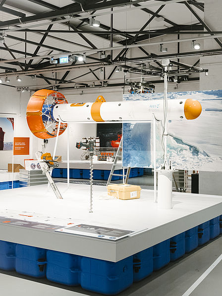 In einer AusstellungshAuf einem Podest werden mehrere Geräte ausgestellt: Eine große Sonde, eine Kettensäge, ein großer Bohrer und weitere Messgeräte. 