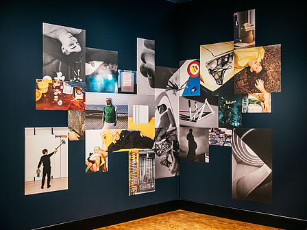 Ein Mosaik aus Fotos hängt an einer dunkelblauen Wand. Auf den einzelnen Fotos sind Bezüge untereinander erkennbar.