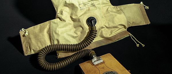 An dem Gasjäckchen mit Sichtfenster ist mit einem Schlauch eine Luftpumpe mit Blasebalg angebracht.