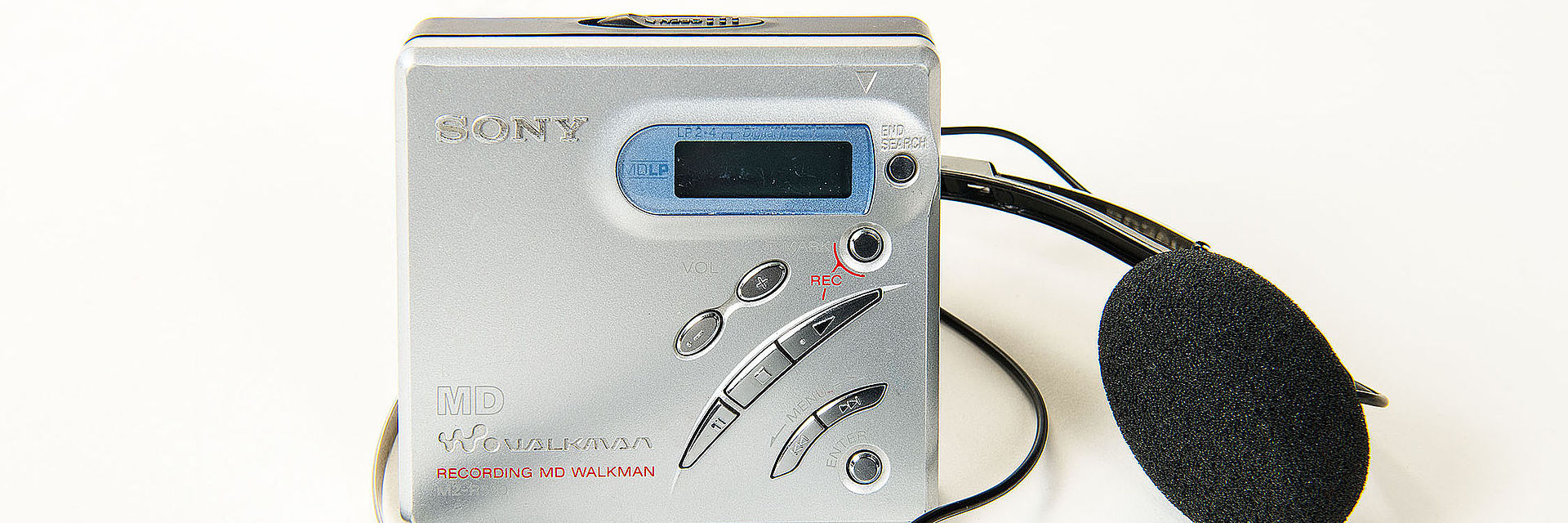Dieser MiniDisc-Rekorder MZ-R500 hat die Form eines kleinen quadratischen Kästchens mit schräg angeordneten Funktionstasten und silbern gefärbter Oberfläche aus Aluminium.