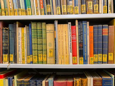 Blick in ein Regal, in dem bunte Buchrücken zu sehen sind, die mit gelben Signaturen ausgestattet sind.