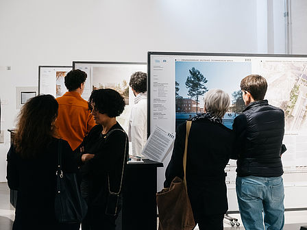 Menschen betrachten verschiedene Architekturenwtürfe an Stellwänden.