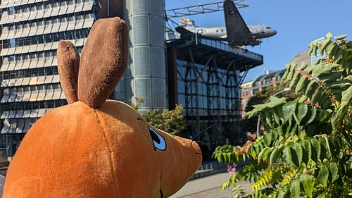 Die Maus blickt aus der Entfernung auf das Deutsche Technikmuseum mit dem Rosinenbomber im Hintergrund 