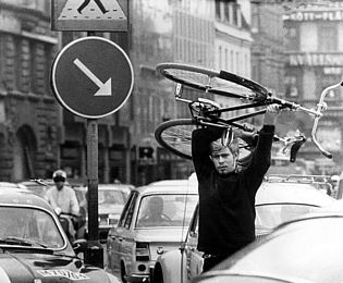 A man lifts a bicycle above his head. He is walking between cars stuck in a traffic jam. The black-and-white photo was taken in Malmö on 3 September 1967. On this day, Sweden switched from left-hand to right-hand traffic. This caused problems and traffic jams in parts of the country.